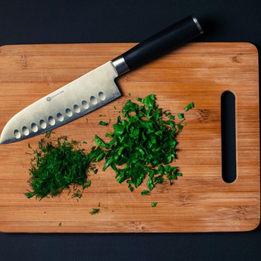 Chef knife and chopped herbs on a bamboo cutting board