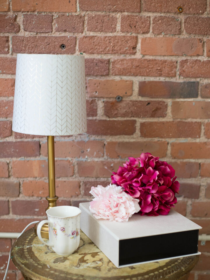 Brass table lamp with a white shade next to a mug and pink flowers